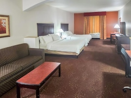 Een hotelkamer met een bank, een kleintje tafeltje, een bed met twee kussens, een bureau met een lamp en een televisietoestel.