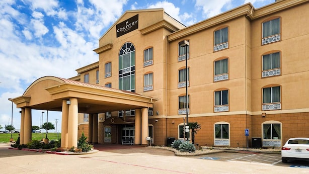 A hotel with a covered entrance, multiple windows, and a sign indicating it is a country hotel. - Country Inn & Suites by Radisson, Terrell (Terrell)