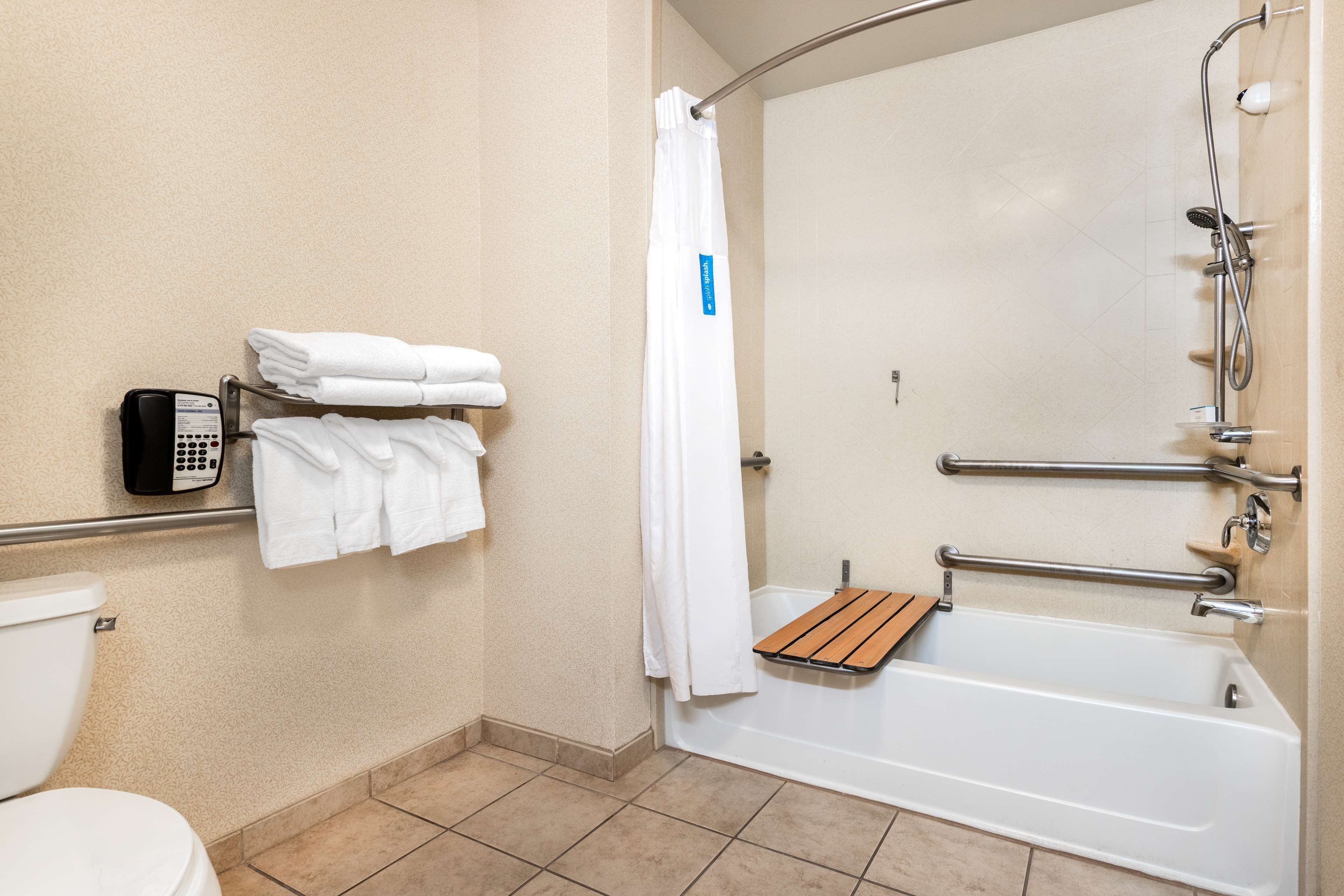 Un bagno con il water, una doccia dotata di maniglione e un portasciugamani con asciugamani piegati.