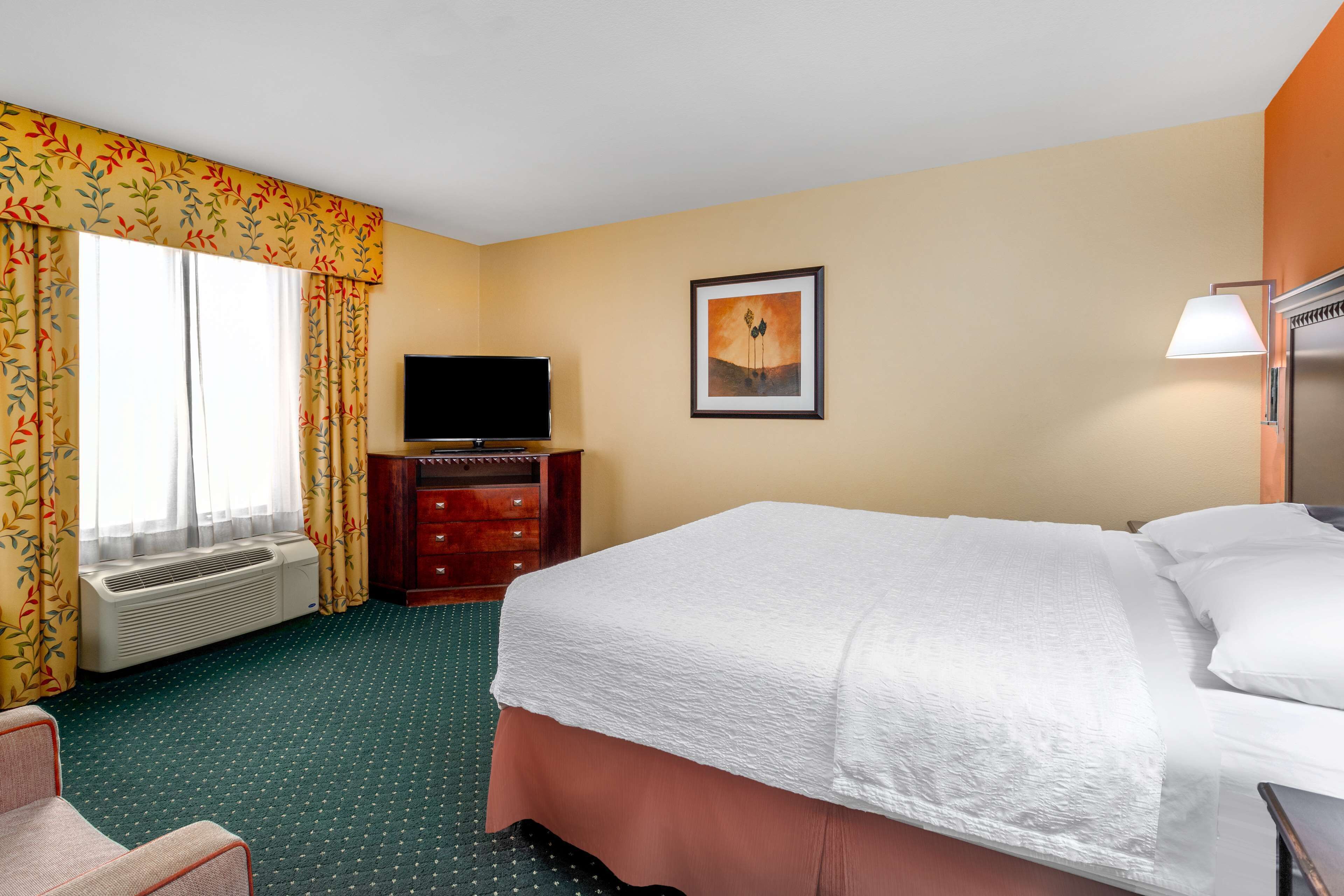 A hotel room with a bed, a television, a dresser, and a painting on the wall.