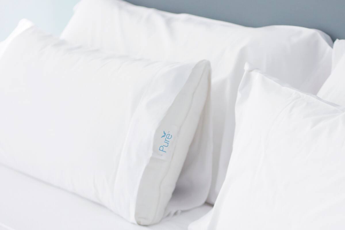 Un lit blanc avec des oreillers, dont l’un porte une étiquette sur laquelle est écrit « Pur ».
