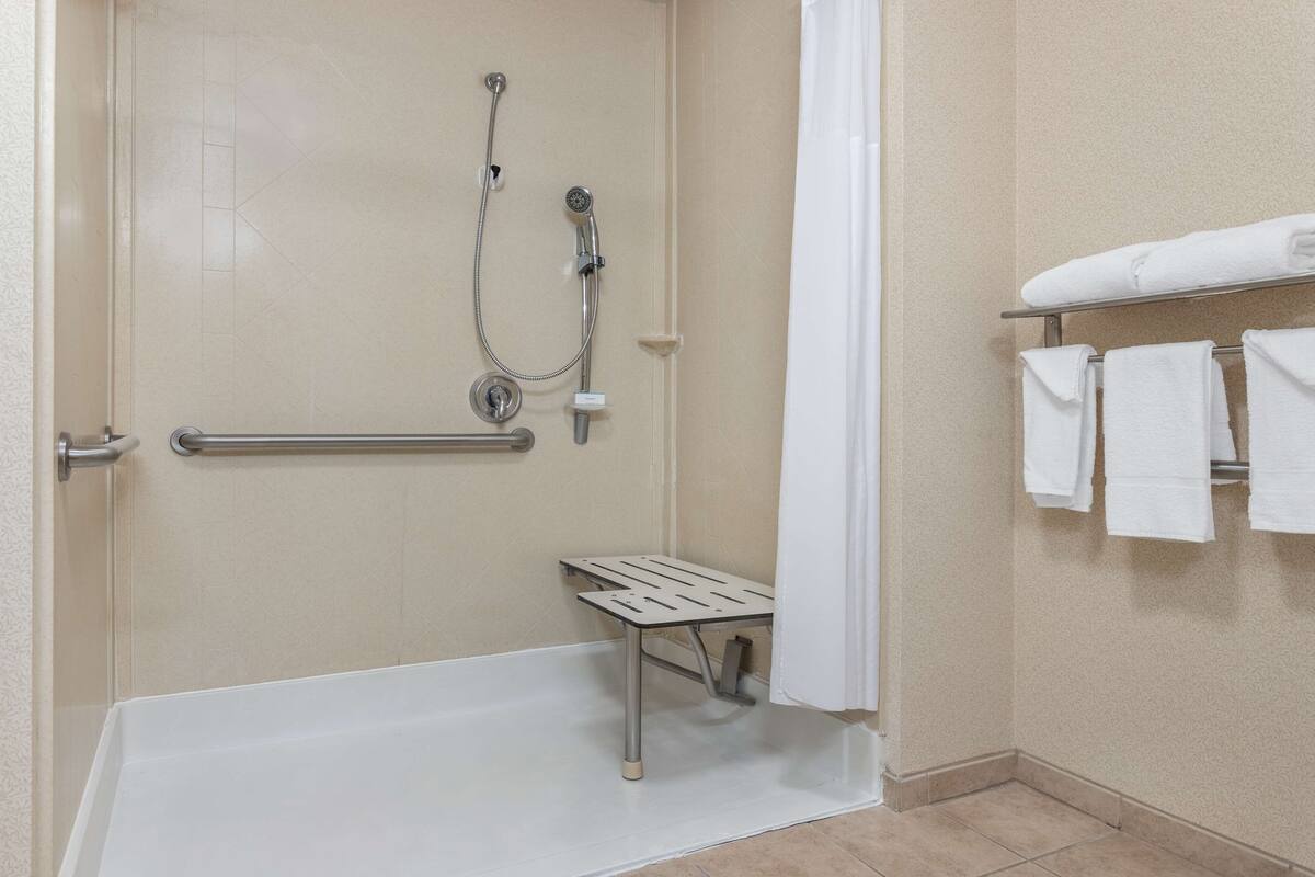 Un espace douche équipé d’une barre d’appui, d’un pommeau de douche, d’un porte-serviettes avec des serviettes et d’un siège de douche.