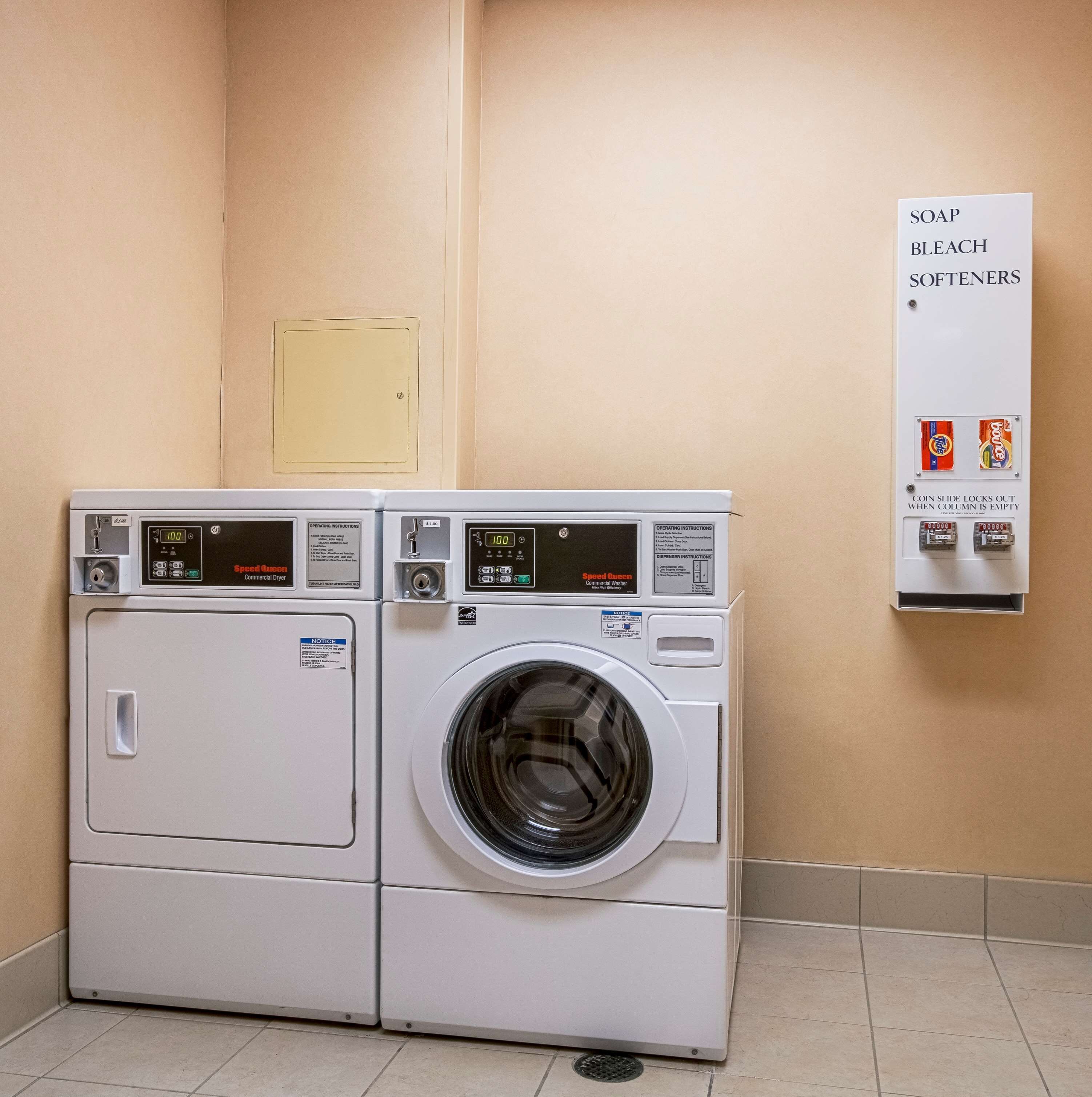 A pair of Speed Queen commercial washers in a utility room with a sign above listing available detergents.