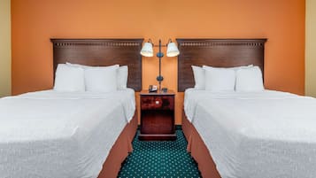 A hotel room with two beds, a nightstand with a lamp, and a green patterned carpet.