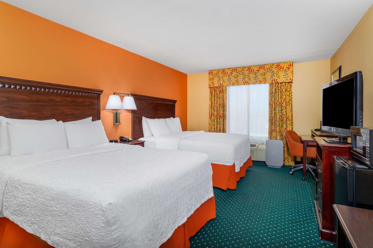 Une chambre d’hôtel avec deux lits, un bureau avec une télévision et une grande fenêtre avec des rideaux.