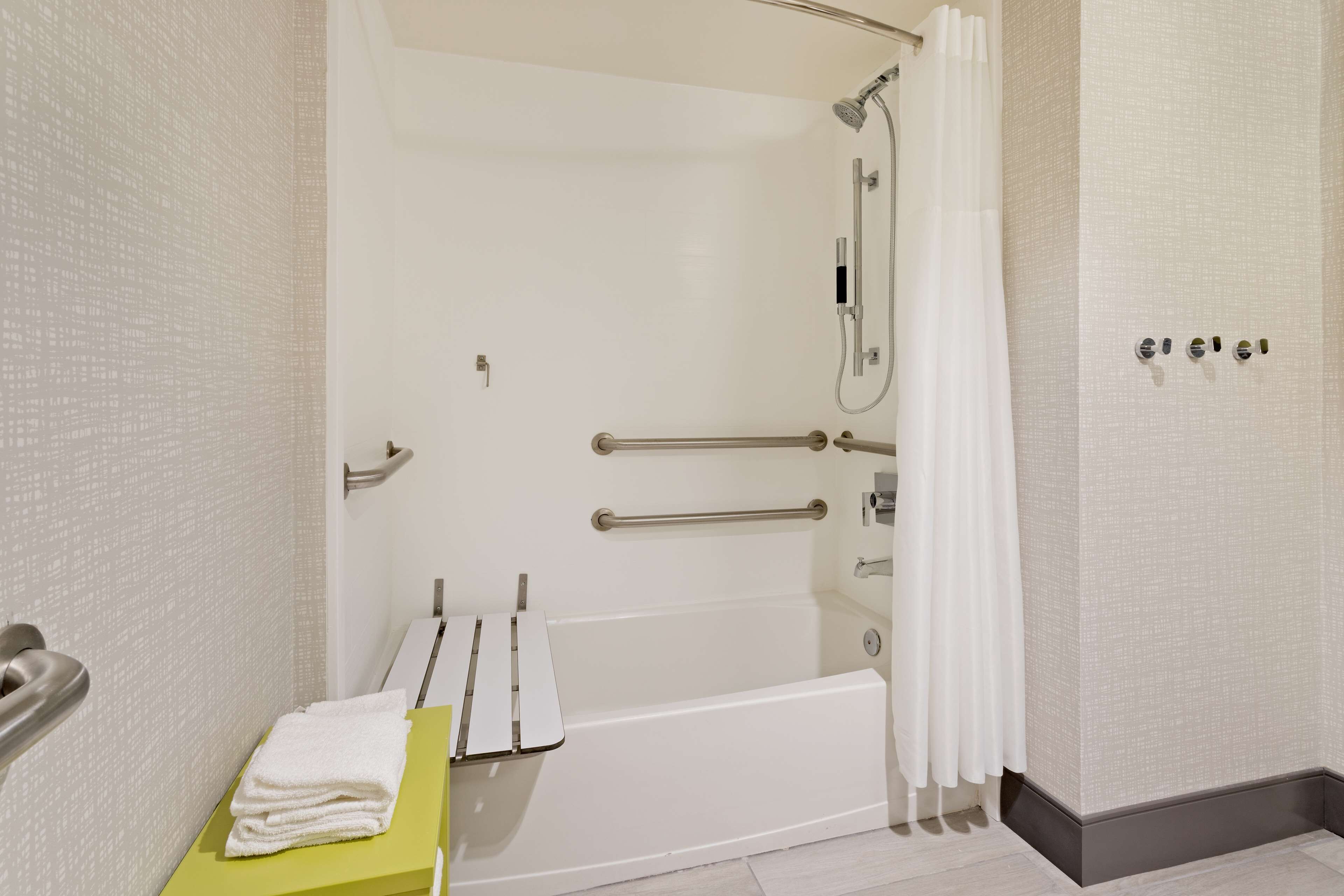 A modern bathroom with a bathtub, a shower, and a toilet. There are grab bars installed for safety, and a towel rack is visible.