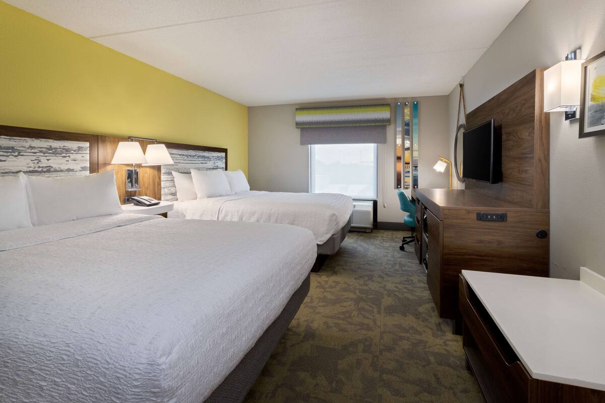 Une chambre d’hôtel avec deux lits, un bureau, une télévision et une fenêtre donnant sur un paysage agréable.