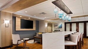 A modern hotel lobby with a marble reception desk, comfortable seating, a flat-screen TV, and a large painting on the wall. - Hampton Inn Jacksonville-I-295 East/Baymeadows (Jacksonville)