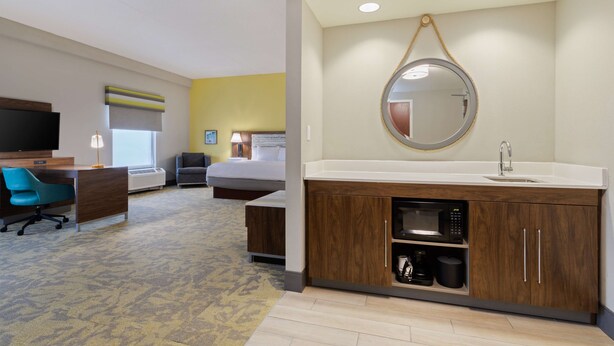 A hotel room with a large bed, a desk with a chair, a TV, a bathroom with a sink and mirror, and a carpeted floor. - Hampton Inn Jacksonville-I-295 East/Baymeadows (Jacksonville)