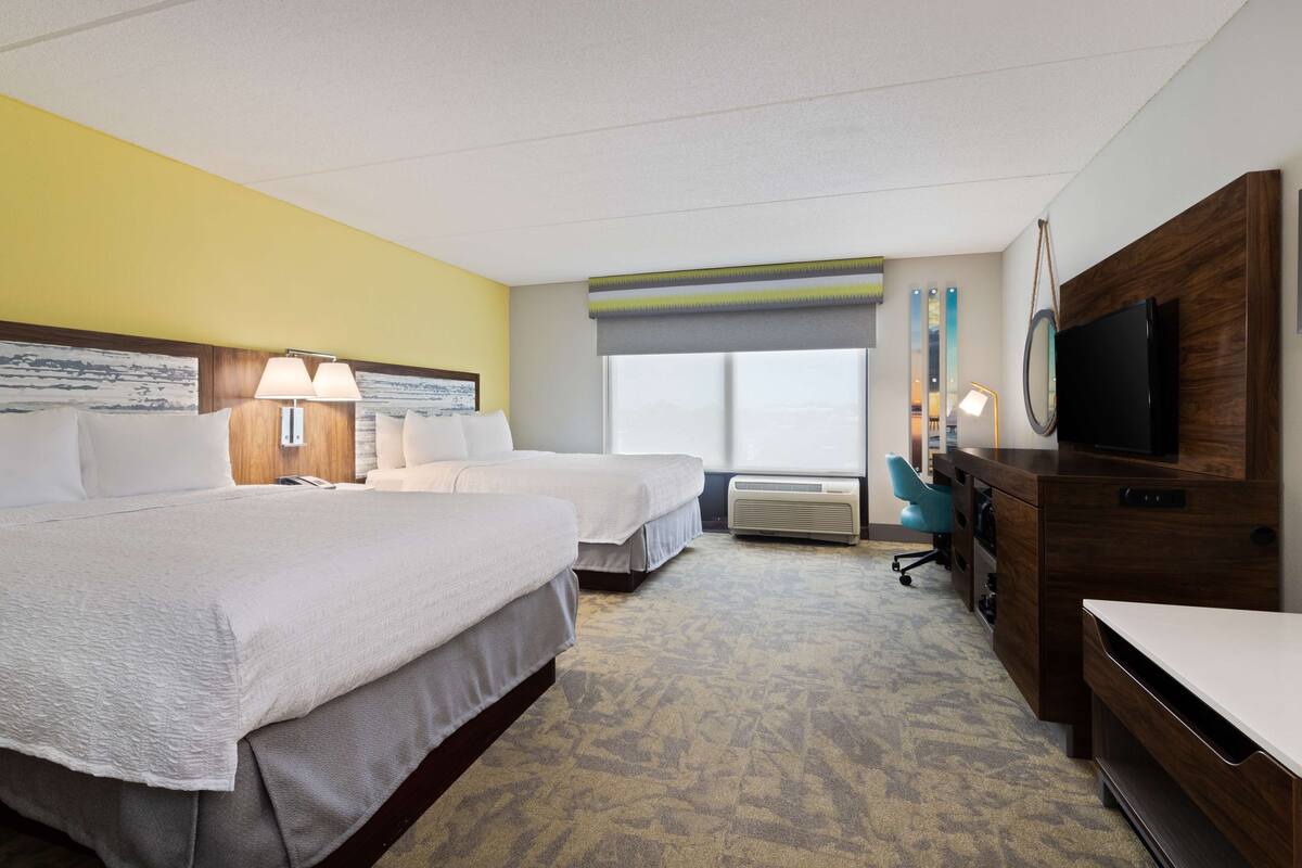 Une chambre d’hôtel avec deux lits, un bureau, une télévision et une grande fenêtre.