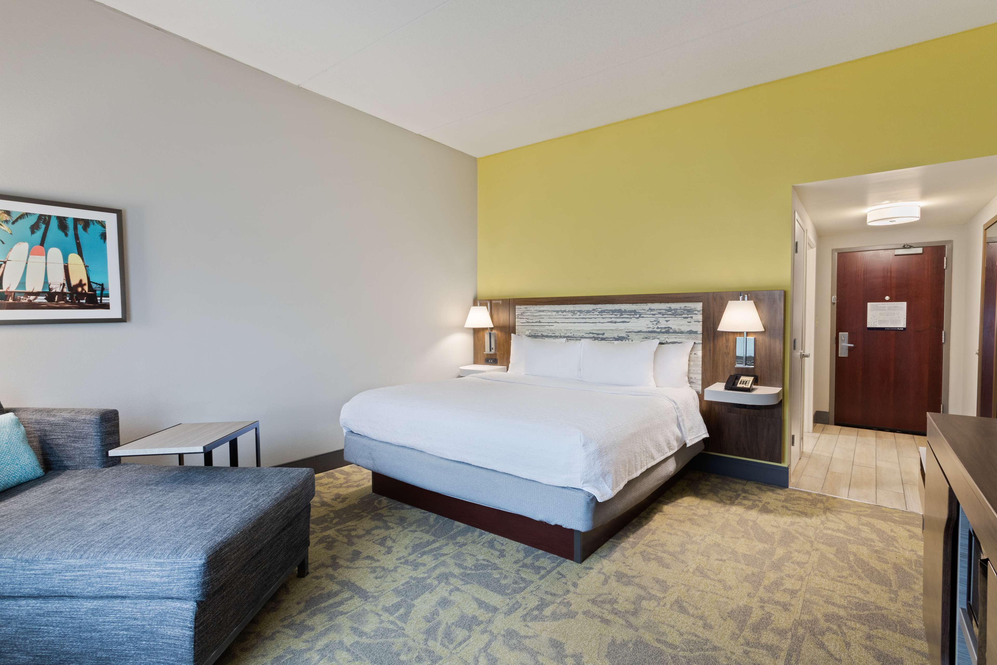 A hotel room with a bed, a small table, a couch, and a painting on the wall.