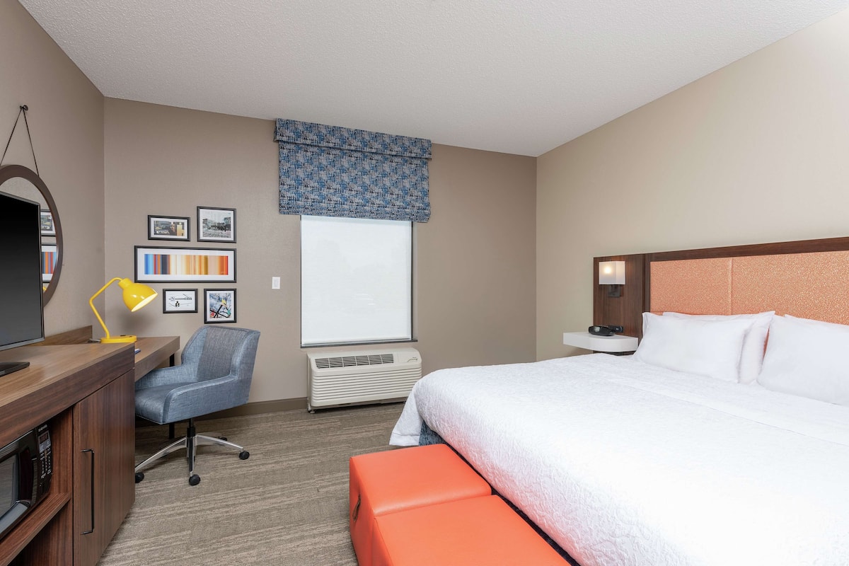 A hotel room with a bed, desk, chair, and a window with blinds.