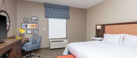 A hotel room with a bed, desk, chair, and a window with blinds.