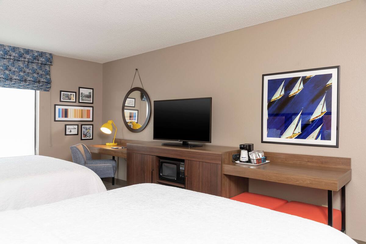A hotel room with two beds, a desk with a computer, a TV, a microwave, and a coffee machine.