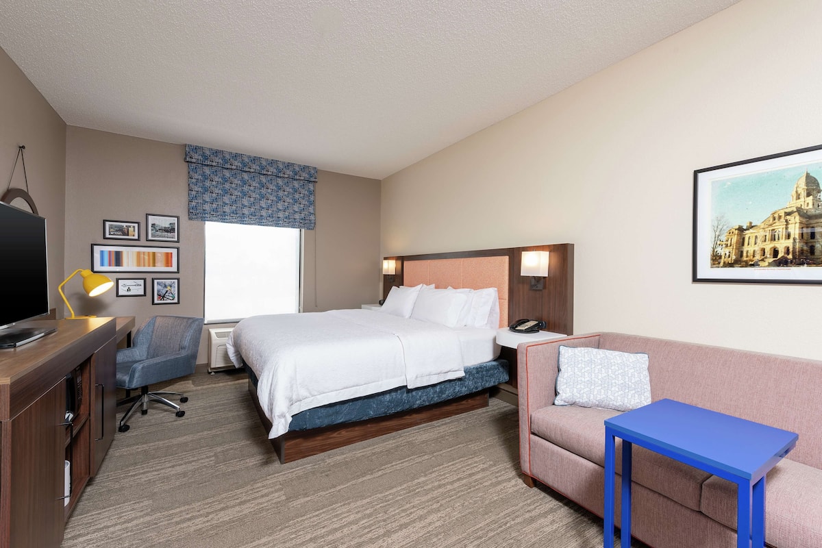 A hotel room with a bed, a desk, a chair, a small table, and a couch.