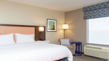 Una habitación de hotel con una cama grande, una mesita de noche, una lámpara, una silla, una pequeña mesa y una ventana con vistas.
