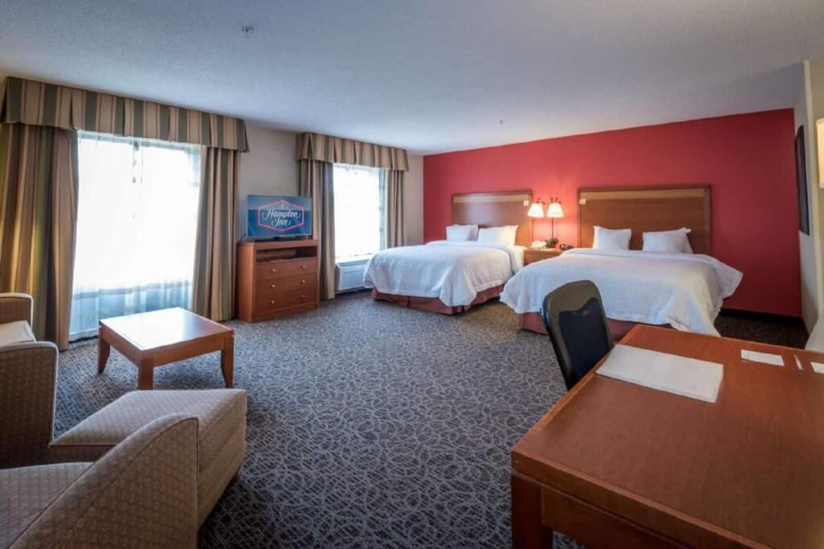 A hotel room with two beds, a desk, a chair, a TV, and a window with curtains.