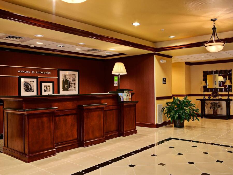 A reception area with a wooden reception desk, framed pictures, a lamp, and a potted plant.