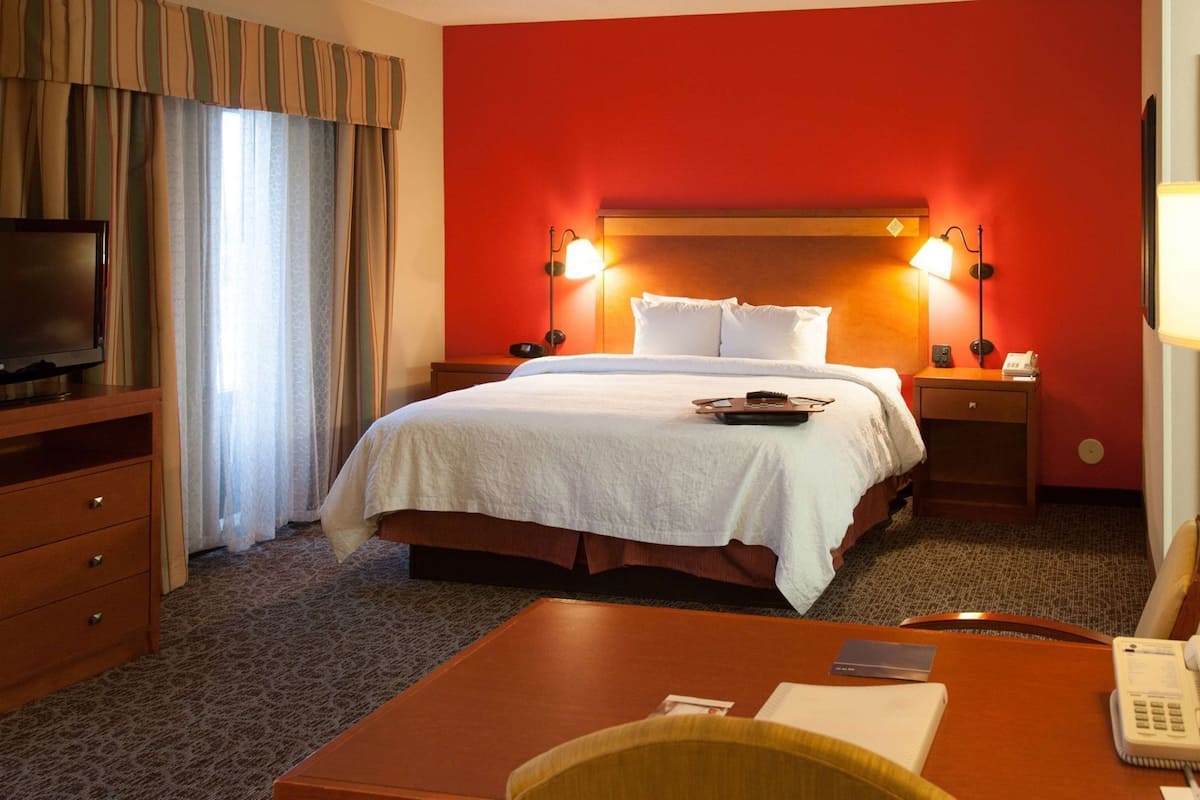 A hotel room with a bed, a desk, a chair, a television, and a telephone.