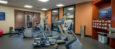 A gym with various exercise machines, a visible Hampton Inn sign, and a wall-mounted sign with motivational text.