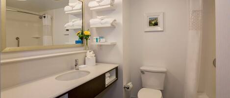 A modern bathroom with a white sink, mirror, and toilet. There are towels and toiletries on the counter, and a shower curtain is visible.