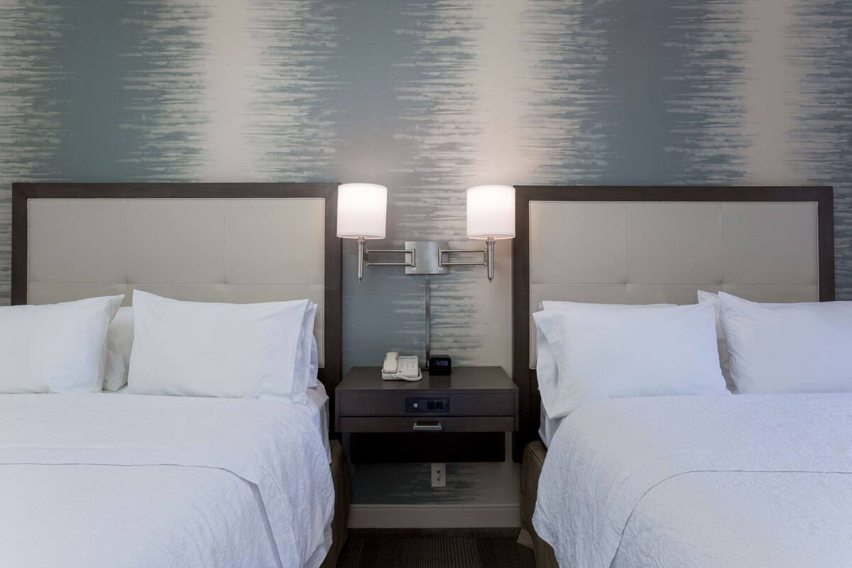 A hotel room with two beds, a nightstand with a phone and clock, and a wall with a textured design.