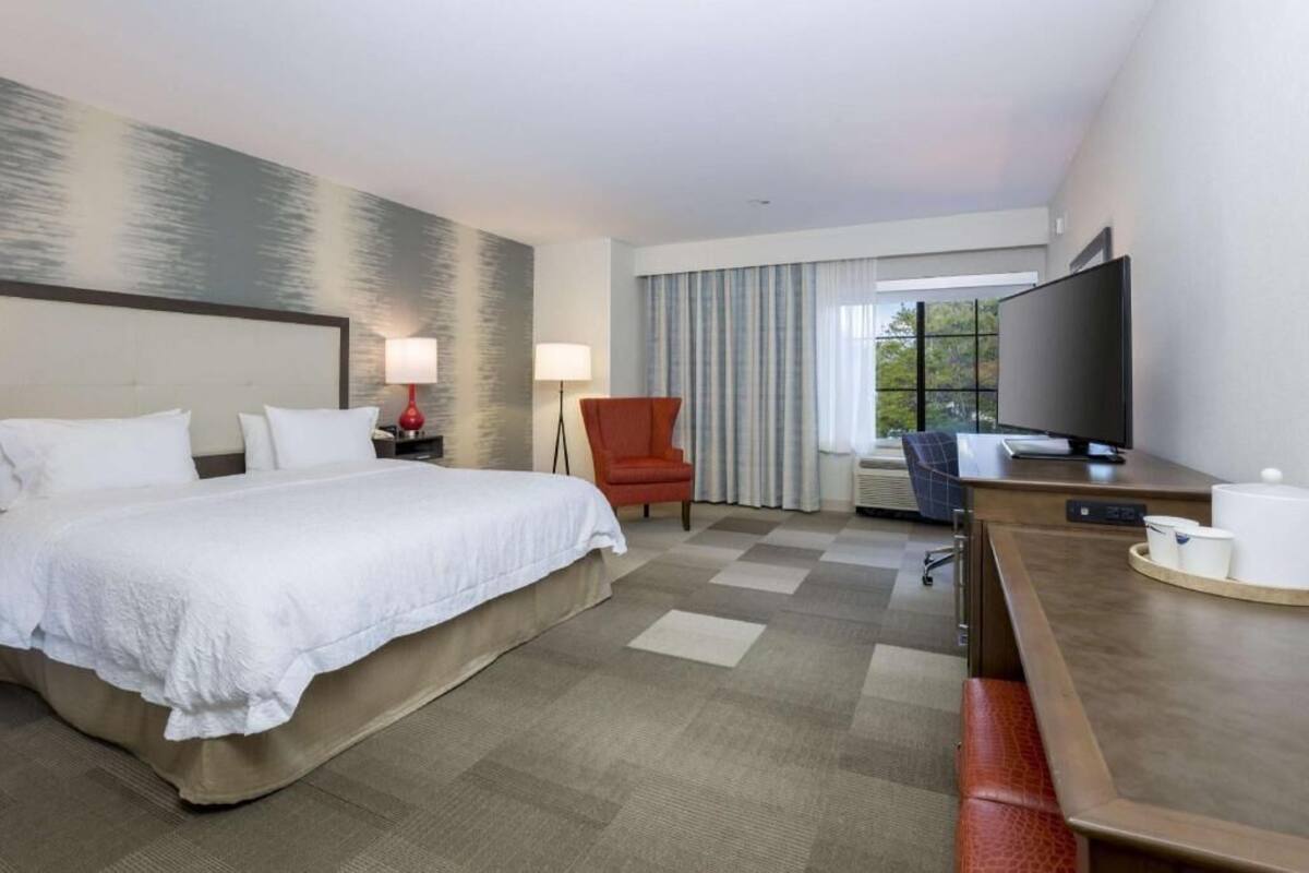 A hotel room with a bed, desk, chair, TV, and a large window.