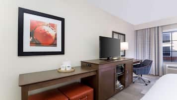 A hotel room with a bed, a desk with a television, a chair, a small table with cups, and a framed picture on the wall.
