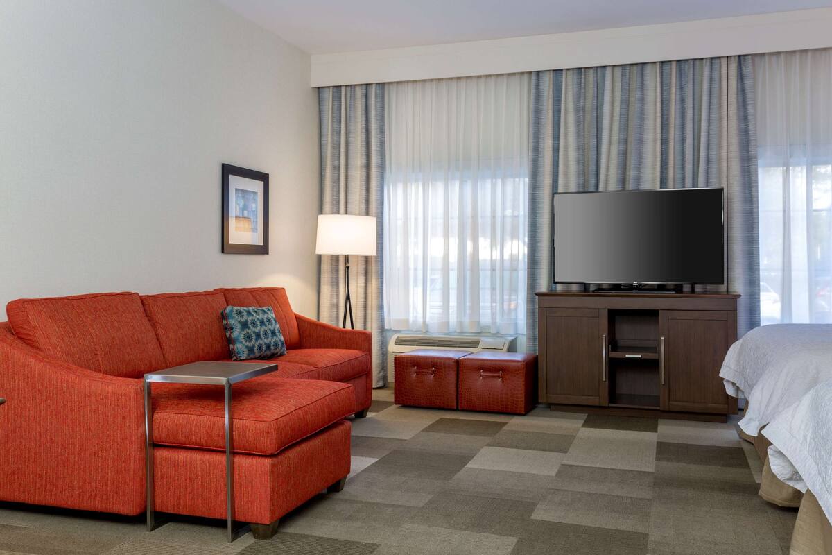 A hotel room with a red sofa, a television, a bed, and a large window with curtains.