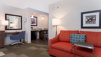 Habitación de hotel con un sofá rojo, un escritorio con una silla, una mesita, un espejo, una lámpara y un cuadro en la pared.