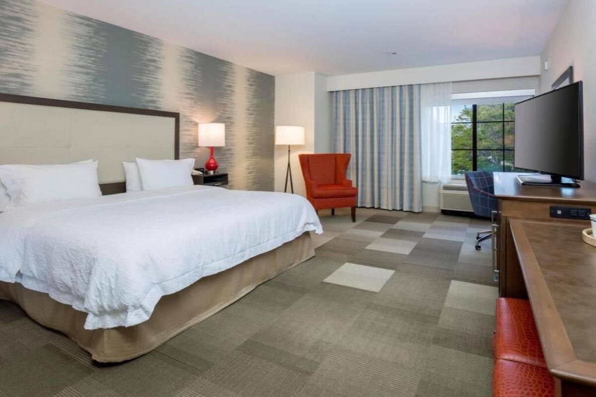 A hotel room with a bed, a desk, a chair, a TV, and a window with curtains.