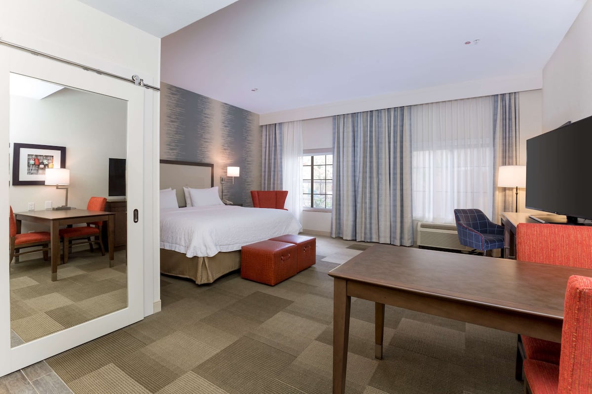 A hotel room with a bed, a desk, a chair, a television, and a large window with curtains.