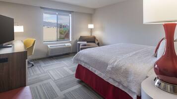 Une chambre d’hôtel avec un lit, un bureau équipé d’un ordinateur, une chaise, une lampe et une fenêtre donnant sur les montagnes.