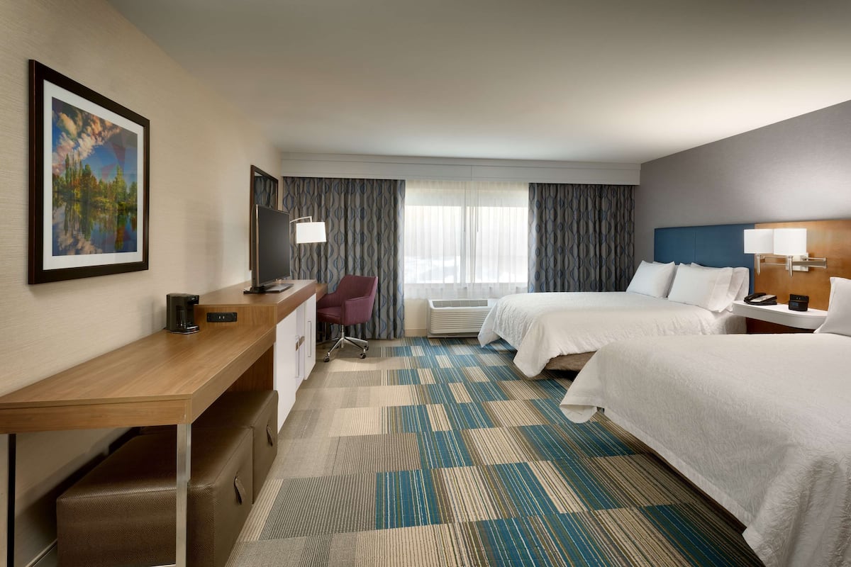 A hotel room with two beds, a desk, a chair, a TV, and a window with curtains.