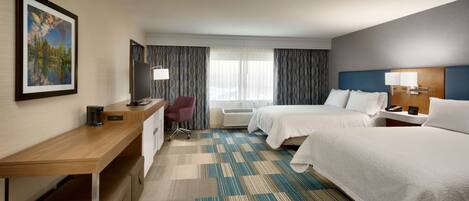 A hotel room with two beds, a desk, a chair, a TV, and a window with curtains.