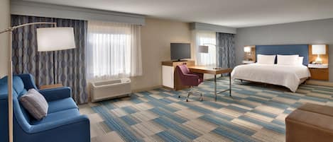 Una habitación de hotel con cama, escritorio, silla, televisión y sofá.