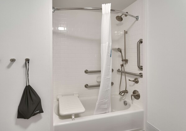 A modern bathroom with a walk-in shower, grab bars, and a white tiled wall.