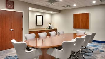 A conference room with a wooden table, white chairs, a clock, and a framed abstract art piece on the wall.