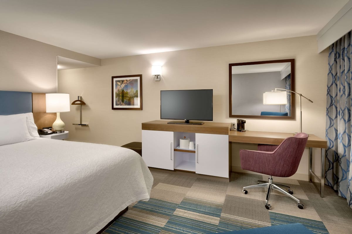 A hotel room with a bed, desk, chair, television, and a large mirror.