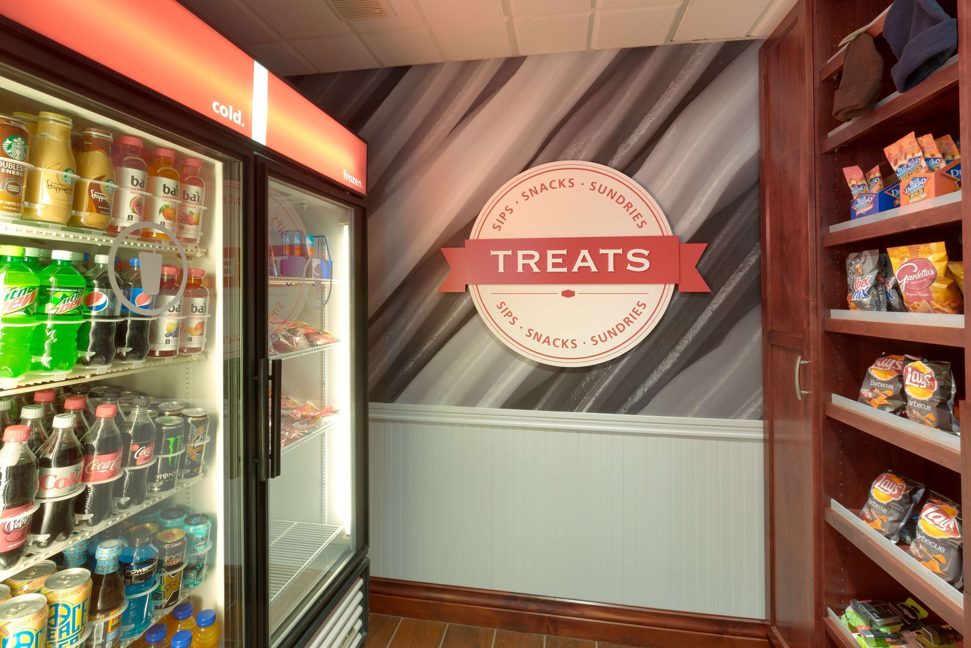 A refrigerated display case filled with beverages and snacks, with a sign indicating a treats section.
