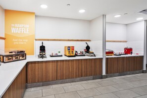 Ein sauberer, moderner Küchenbereich mit einem Waffelautomaten, einer Kaffeemaschine und einer Vitrine mit Waffeln.