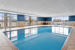 An indoor swimming pool with clear blue water, surrounded by a tiled floor and walls, with a seating area and a view of the outside. - Hampton Inn & Suites Omaha Southwest-La Vista (La Vista)