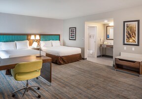 Una habitación de hotel con una cama, un escritorio, una silla, un baño y un cuadro en la pared.
