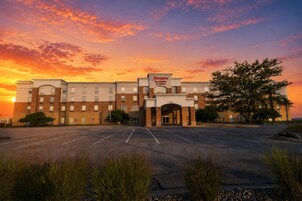 Hotel Hampton Inn & Suites by Hilton con estacionamiento y un atardecer de fondo.