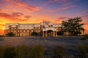 Hotel Hampton Inn & Suites by Hilton con estacionamiento y un atardecer de fondo.