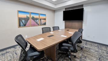 A conference room with a long table, six chairs, a flat-screen TV, and two paintings on the wall.
