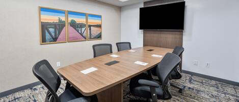 Un salón de conferencias con una larga mesa, seis sillas, un televisor de pantalla plana y dos cuadros en la pared.