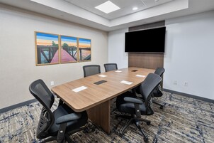 A conference room with a long table, six chairs, a flat-screen TV, and two paintings on the wall.