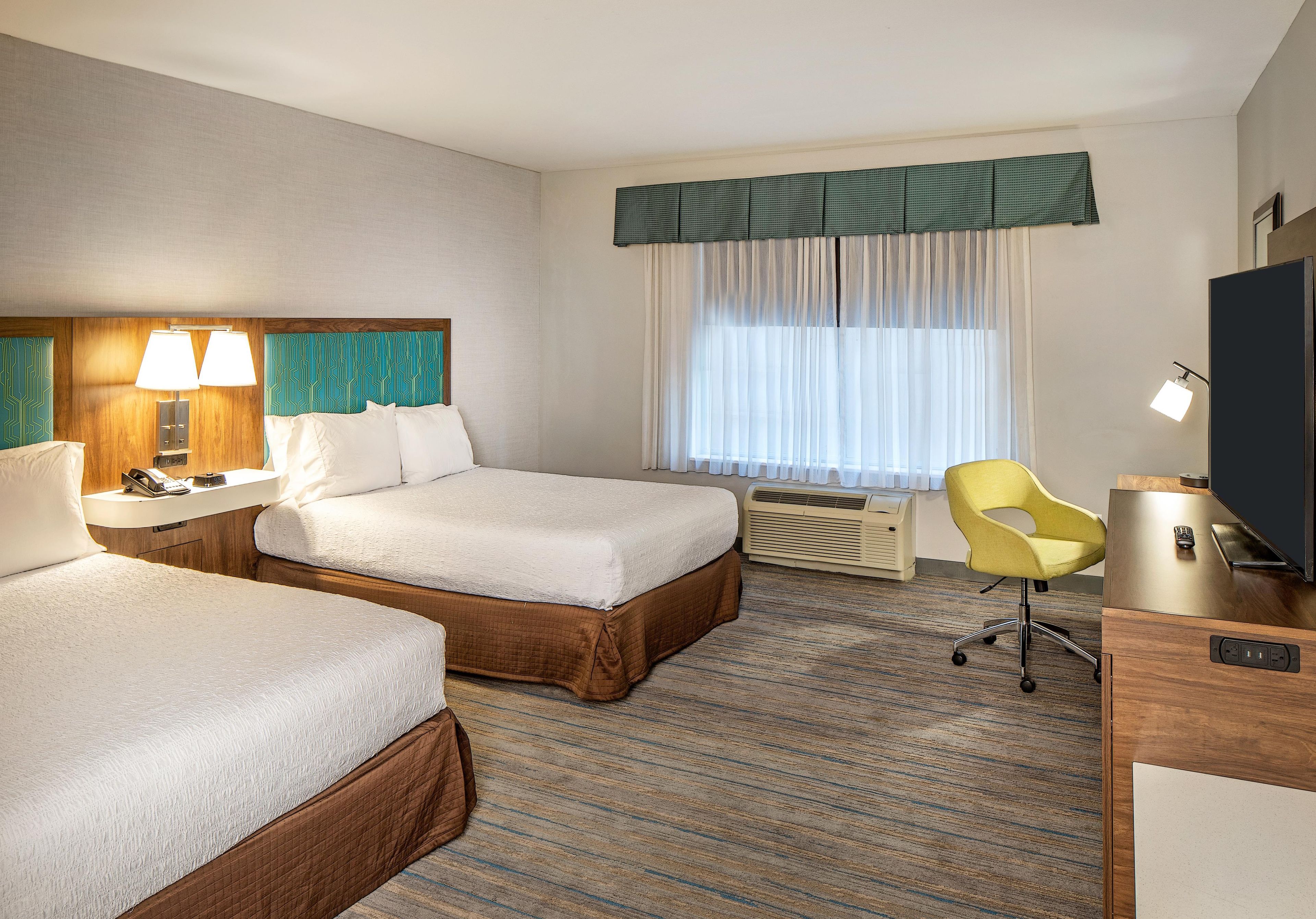 A hotel room with two beds, a desk, a chair, a television, and a window with curtains.