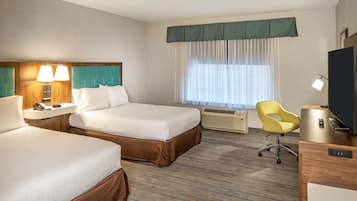 A hotel room with two beds, a desk, a chair, a television, and a window with curtains.